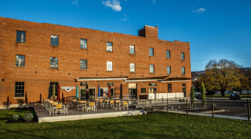 A brick building with a patio area, featuring outdoor seating and a clear blue sky in the background.