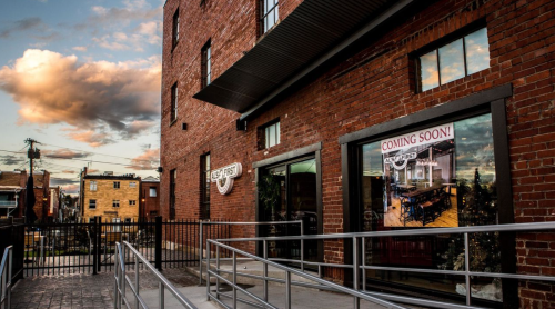 Exterior of a brick building with large windows, featuring a "Coming Soon!" sign and a ramp for accessibility.
