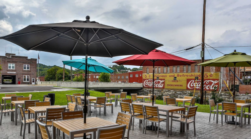 Outdoor seating area with colorful umbrellas and tables, overlooking a historic Coca-Cola mural in a small town.