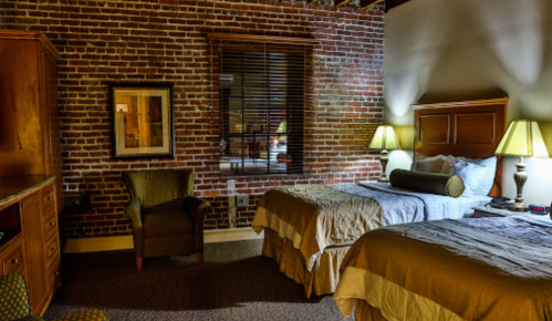 Cozy hotel room with two beds, brick walls, a chair, and warm lighting.