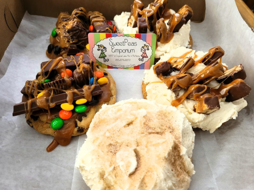 Four decorated cookies with various toppings, including chocolate, caramel, and candy, alongside a business card.