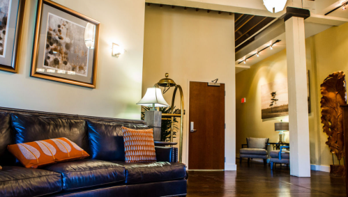 A cozy interior featuring a leather sofa with decorative pillows, warm lighting, and artwork on the walls.