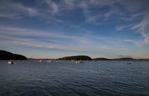 A serene seascape with boats on calm water, surrounded by distant islands and a clear blue sky.