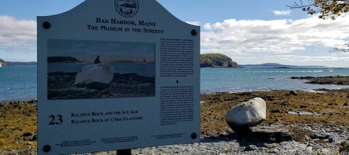 Sign about Balance Rock in Bar Harbor, Maine, with a scenic view of the ocean and coastline in the background.
