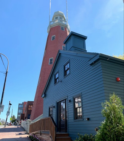 A tall red lighthouse beside a blue house, set against a clear blue sky.