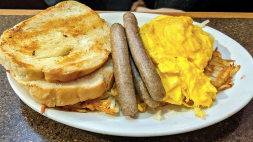 A plate with two slices of toasted bread, three sausage links, scrambled eggs, and hash browns.