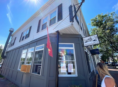 A corner view of Hilltop Coffee, featuring a flag and large windows on a sunny day.