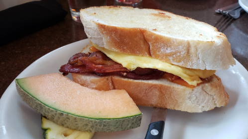 A sandwich with bacon, cheese, and an egg, served with slices of cantaloupe on the side.