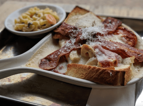 A plate of baked pasta with bacon on toast, served with a side of macaroni salad.