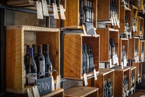 Wooden shelves display various wine bottles, each labeled with tags, showcasing a selection from different regions.