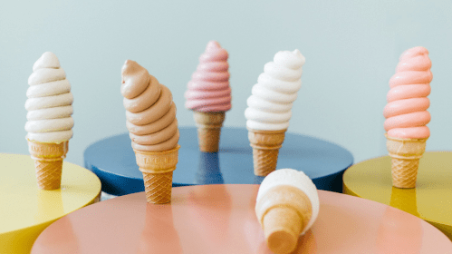 A variety of ice cream cones with swirled toppings in different colors, displayed on colorful circular surfaces.