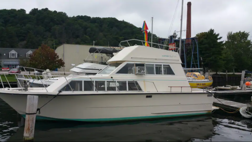 A white cabin cruiser boat docked at a marina, surrounded by other boats and green hills in the background.