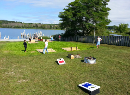 People setting up games on a grassy area by a lake, with wooden platforms and a dock in the background.