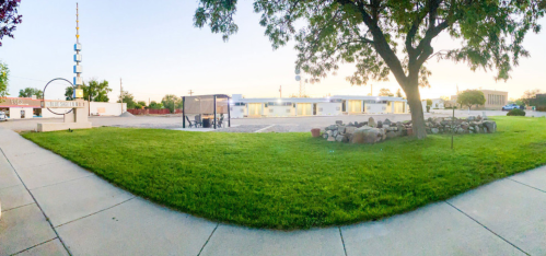 A grassy area with a bus stop, surrounded by buildings and trees, under a clear sky at sunset.