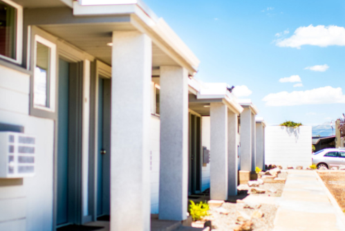 A row of modern, minimalist houses with light blue doors and a clear blue sky in the background.