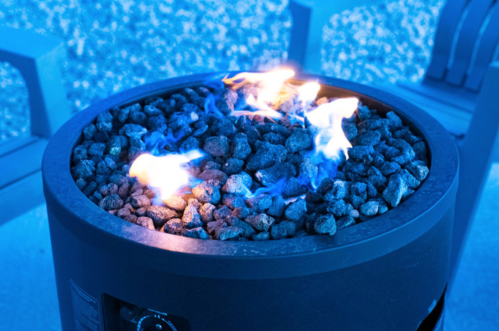A close-up of a modern fire pit with blue flames flickering over dark rocks.