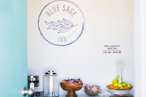 A cozy breakfast area at Blue Sage Inn with snacks, fruits, and a sign displaying breakfast hours.