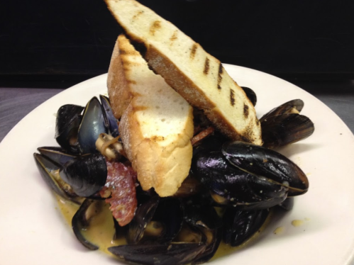 A plate of mussels topped with grilled bread, garnished with herbs in a savory broth.