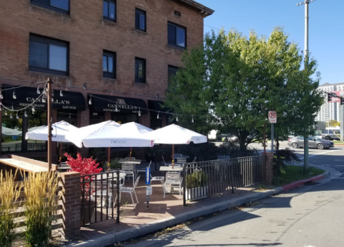 Outdoor dining area with umbrellas at a restaurant, surrounded by greenery and a brick building.