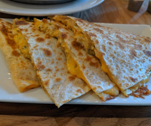 A plate of golden-brown quesadillas filled with melted cheese, cut into wedges, served on a white dish.