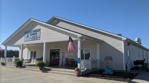 Exterior of Black Sheep Diner, featuring a porch, American flags, and a clear blue sky.