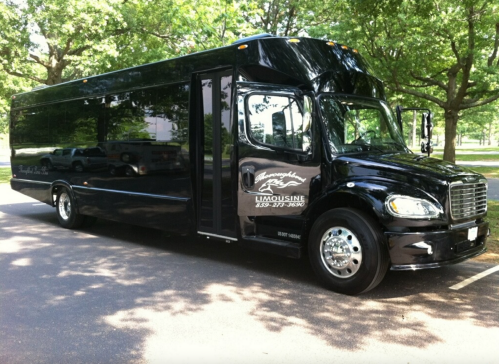 A black limousine bus parked on a tree-lined street, showcasing its sleek design and spacious exterior.