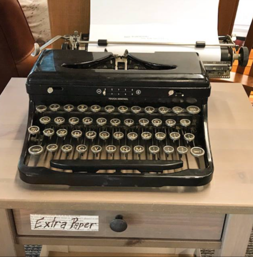 A vintage black typewriter on a wooden table with a sign that reads "Extra Paper."