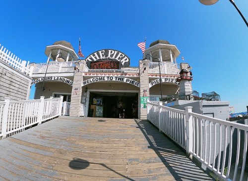 A wooden pier entrance with a sign reading "The Pier" and flags, under a clear blue sky.