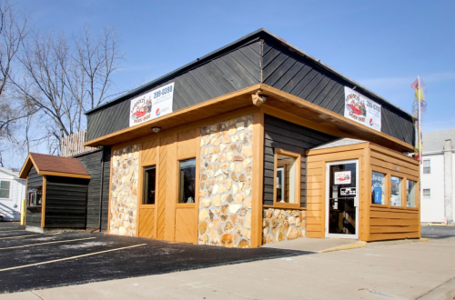 A small restaurant with a stone and wooden exterior, featuring large windows and signage on the walls.