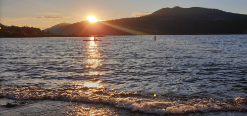 Sunset over a calm lake, with shimmering water and mountains in the background.