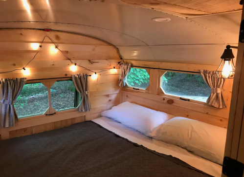 Cozy interior of a camper with wooden walls, string lights, and a bed with white pillows and gray bedding.
