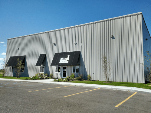 A modern gray building with black awnings and a landscaped entrance, set against a clear blue sky.