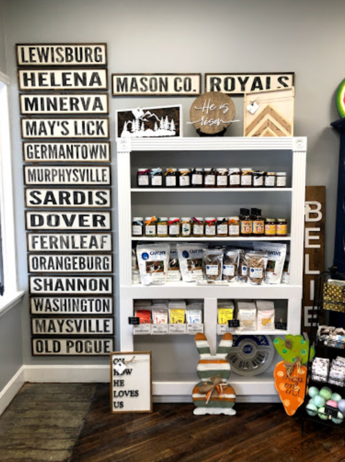A display shelf with various jars and packages, surrounded by decorative signs featuring town names and inspirational messages.