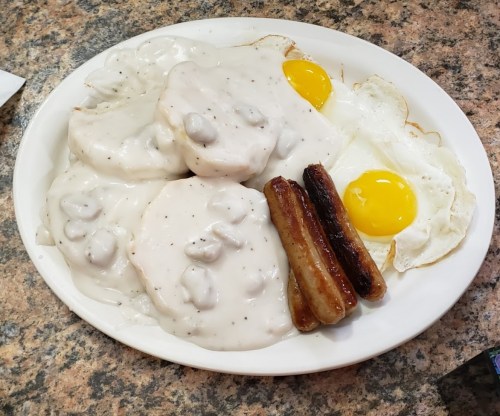 A plate of biscuits and gravy, two fried eggs, and sausage links on a granite countertop.
