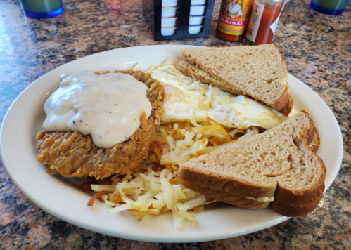 A plate of chicken fried steak with gravy, eggs, hash browns, and two slices of toast on a diner table.