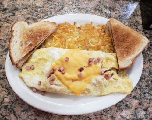 A plate with a cheese omelet topped with ham, crispy hash browns, and two slices of toasted bread.