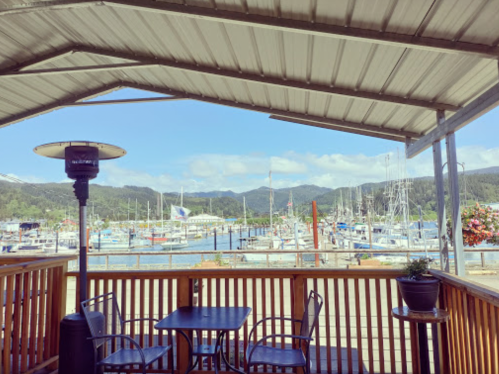 A view of a marina with boats, mountains in the background, and a covered patio with tables and a heater.