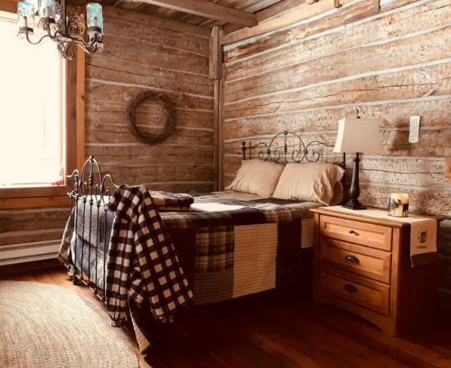 Cozy rustic bedroom with a wooden wall, a bed with plaid bedding, a nightstand, and a warm atmosphere.