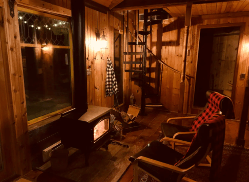 Cozy wooden interior with a spiral staircase, a fireplace, and two chairs, creating a warm, inviting atmosphere.
