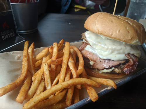 A hearty burger with melted cheese and layers of meat, served with a side of crispy French fries on a metal tray.