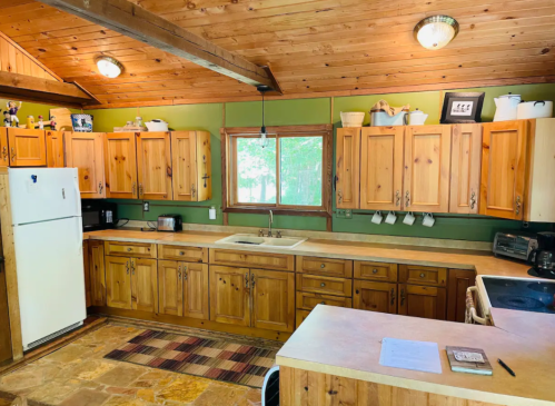 Cozy wooden kitchen with green walls, natural light, and ample cabinetry, featuring a sink and appliances.