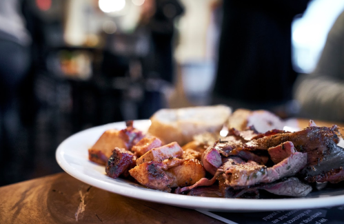 A close-up of a plate featuring sliced meats and roasted potatoes, with a soft roll on the side.