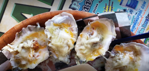 A wooden plate with four baked oysters topped with melted cheese and a hint of seasoning.