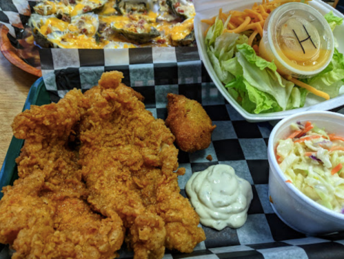 A plate of fried chicken, coleslaw, a side salad with dressing, and a cornbread muffin on a checkered tray.