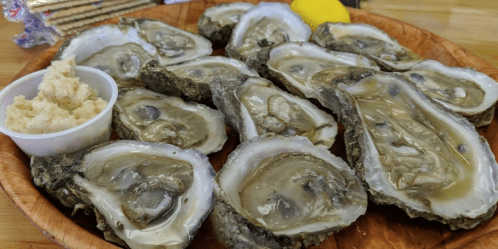 A wooden platter filled with fresh oysters, accompanied by a small cup of horseradish and a lemon wedge.