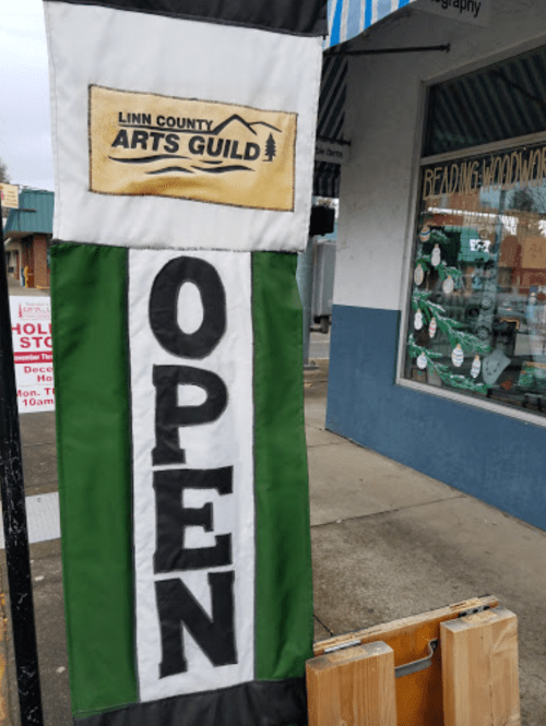 A banner for the Linn County Arts Guild displaying "OPEN" in large letters, outside a storefront.