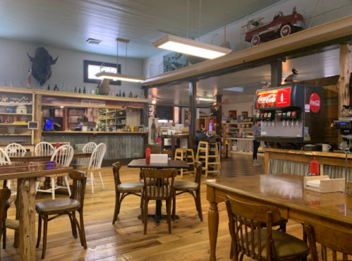 Cozy restaurant interior with wooden tables, chairs, and a Coca-Cola fountain machine, featuring rustic decor.