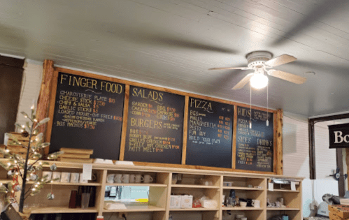 Menu board featuring finger foods, salads, pizza, burgers, and kids' options in a casual dining setting.