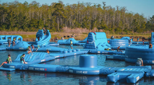 A vibrant water park with inflatable structures, people enjoying activities on the water, surrounded by trees.