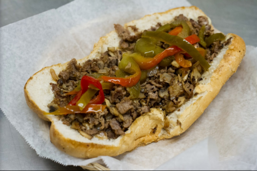 A loaded sandwich with sliced beef, sautéed onions, and colorful peppers on a soft hoagie roll.